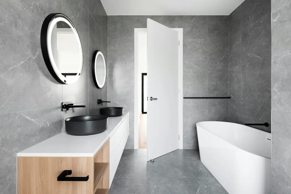 Baño contemporáneo gris con griferías negras, espejo redondo y bañera exenta
